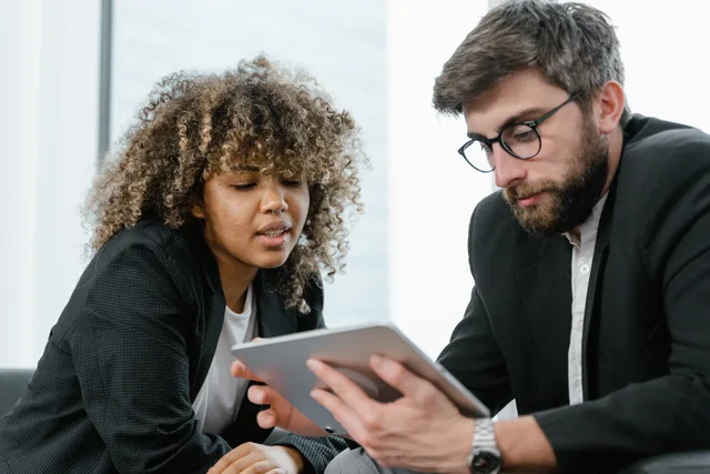 Two business professionals reviewing data on a tablet, fostering collaboration and teamwork in a modern office setting. Kostnadsmodeller för it-tjänster och vad de innehåller
